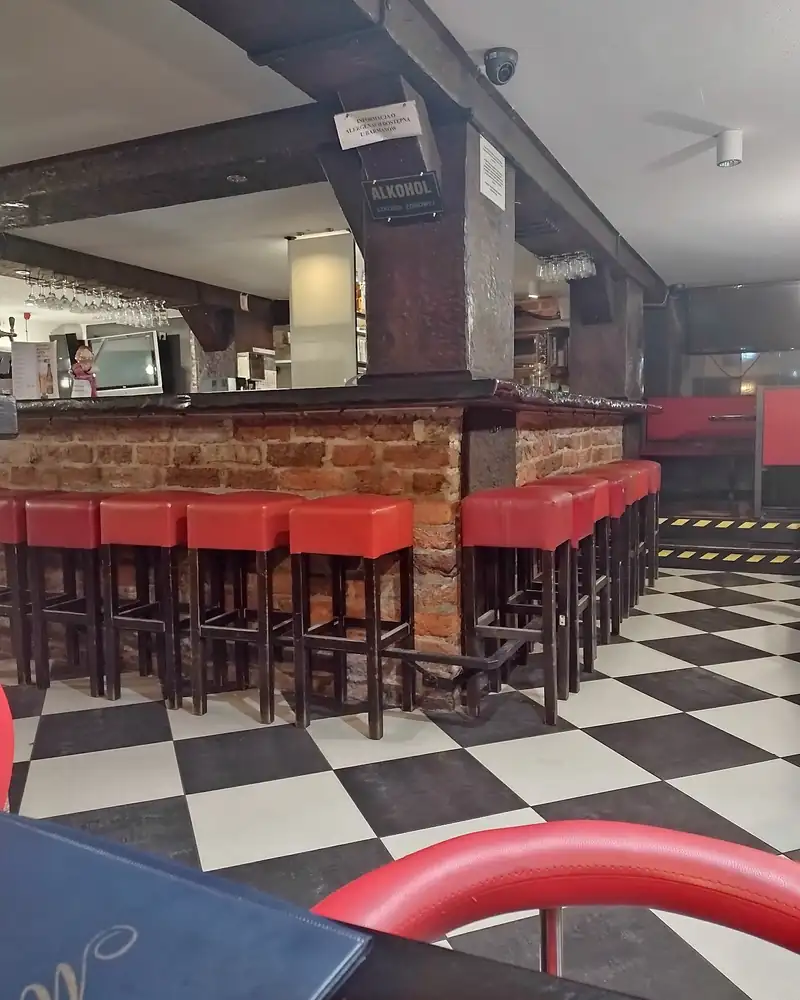Ceglany bar z czerwonymi stołkami i podłoga w czarno-białą szachownicę
