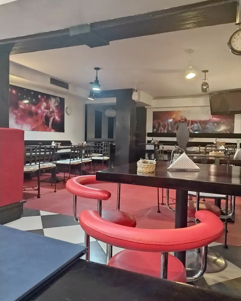 Sala z czerwonymi krzesłami, czarnymi stolikami i podłogą w szachownicę